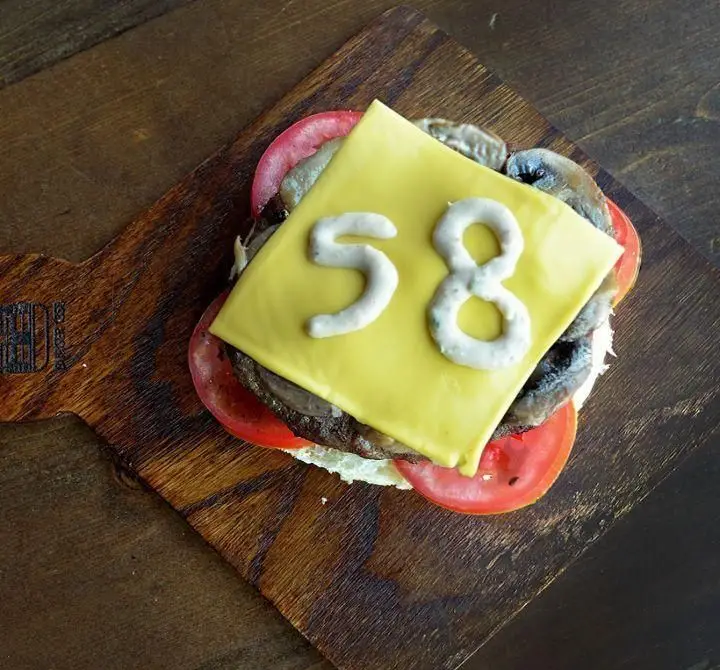 چیزبرگر ویژه و خوش‌طعم برگر ۱۳۵۸ با پنیر، قارچ، گوجه‌فرنگی و عدد ۵۸ روی پنیر، آماده سرو روی میز چوبی.
