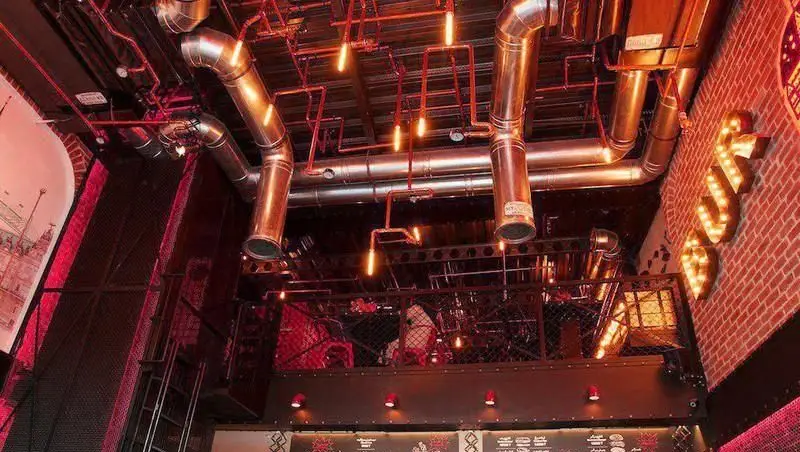 نمای داخلی منحصر به فرد برگر ۱۳۵۸ با دکوراسیون صنعتی، لوله های فلزی، نورپردازی گرم و محیطی دلنشین برای صرف غذا.