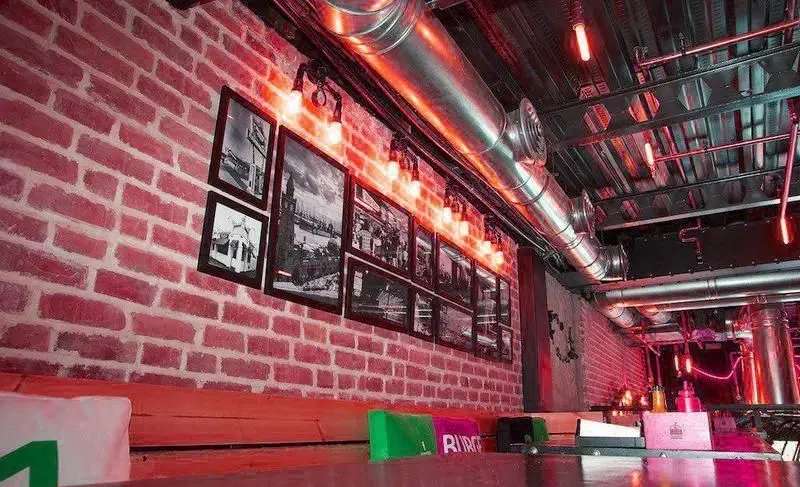 دکوراسیون داخلی رستوران برگر ۱۳۵۸، با دیوار آجری قرمز، تابلوهای سیاه و سفید و طراحی صنعتی مدرن با نورپردازی خاص و دلنشین.