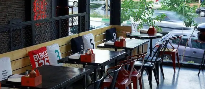 فضای داخلی رستوران برگر ۱۳۵۸ با دکوراسیون صنعتی و مدرن، شامل میز و صندلی‌های شیک و کوسن‌های برندینگ ۱۳۵۸.