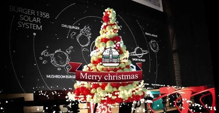 دکوراسیون کریسمس جذاب برگر ۱۳۵۸ با درخت بادکنکی و منوی برگرهای سیاره‌ای. فضای شاد و دلنشین رستوران برای مشتریان.
