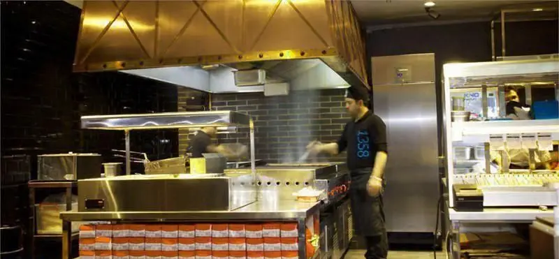 تصویری از آشپزخانه مدرن و تمیز رستوران برگر ۱۳۵۸. سرآشپزهایی در حال پخت برگر بر روی گریل، با تجهیزات حرفه‌ای و محیطی کارآمد.