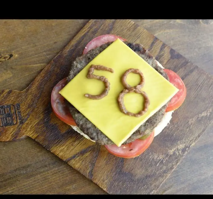 یک برگر خوش‌رنگ از برگر ۱۳۵۸ روی تخته سرو چوبی، با پتی گوشت، گوجه و پنیر زرد که عدد ۵۸ روی آن با سس نقش بسته است.