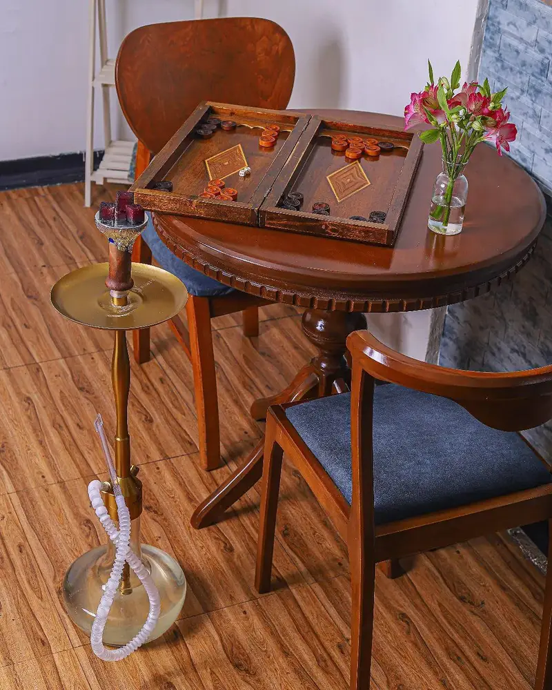 فضای گرم و دنج کافه بینج با میز چوبی زیبا، تخته نرد و قلیان شیک، مکانی عالی برای تفریح و دورهمی‌های دوستانه.