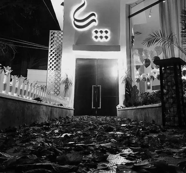 نمای شبانه ورودی کافه رستوران پاپا، با تابلوی درخشان لوگو، مسیر پوشیده از برگهای پاییزی و دکوراسیون داخلی با بادکنک.