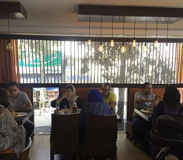 رستوران بان کو: محیطی جذاب با نورپردازی زیبا و مشتریان خوشحال در حال صرف غذا. دکوراسیون مدرن و پنجره‌های رو به خیابان.