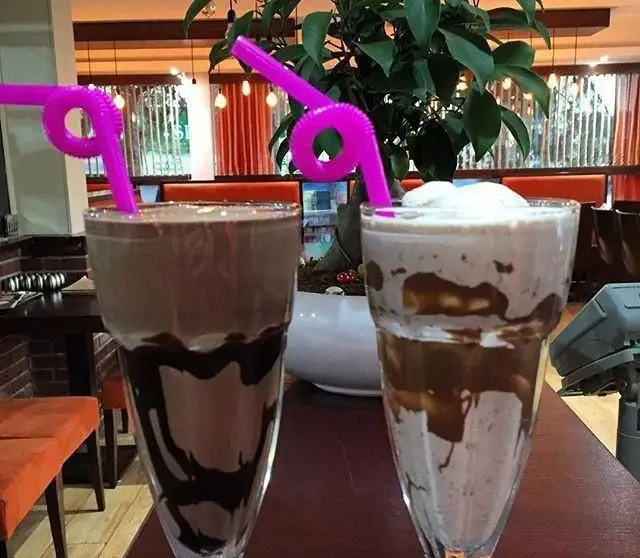 دو میلک شیک مجلل و خنک با طعم‌های شکلاتی و وانیلی، همراه با نی‌های فانتزی صورتی در فضای دلنشین رستوران بان کو، انتخابی عالی.