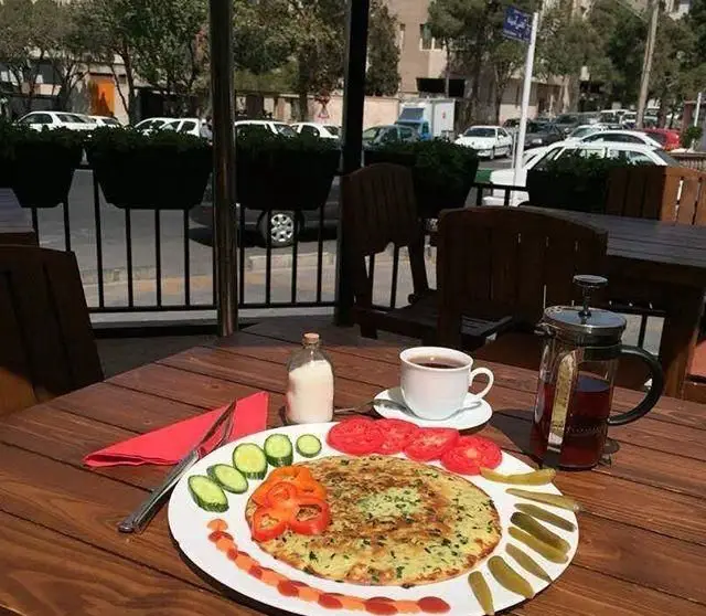 رستوران بان کو: صبحانه‌ای لذت‌بخش با املت ایرانی، چای و قهوه در فضای باز. میزی چوبی، تزئینات زیبا و چشم‌انداز شهری دلنشین.