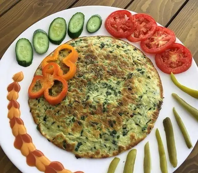 بشقاب کوکو سبزی تازه و خوشمزه رستوران بان کو، با تزئین گوجه، خیار، فلفل و ترشی. انتخابی سالم و کامل برای صبحانه یا ناهار ایرانی.