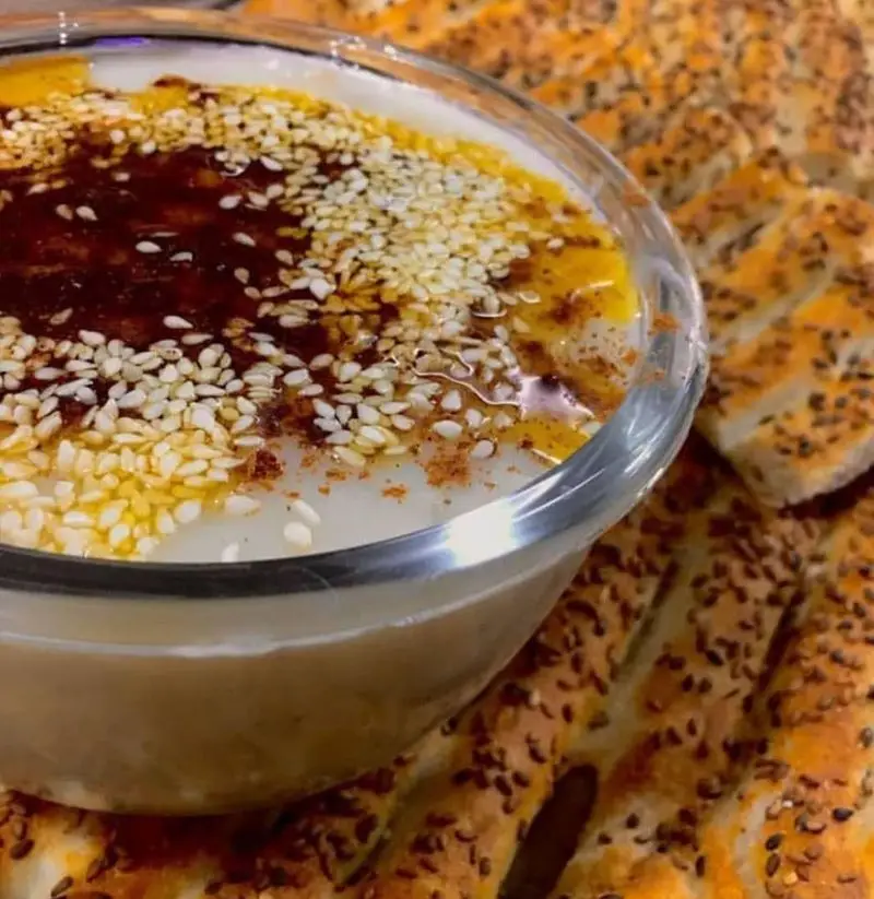 کاسه حمص کرمی با روغن زیتون، کنجد و نان داغ کنجدی خانگی فود شادان. تجربه طعم اصیل در رستوران غذای خونگی.