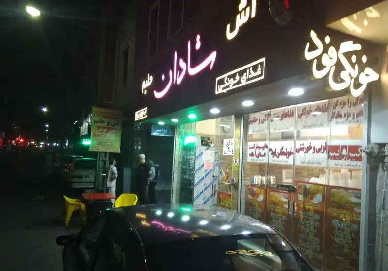 رستوران غذای خونگی فود شادان در شب با تابلوهای نئونی آش، حلیم، انواع غذاهای آماده، پلویی و خورشتی، مناسب سفارش بیرون بر.