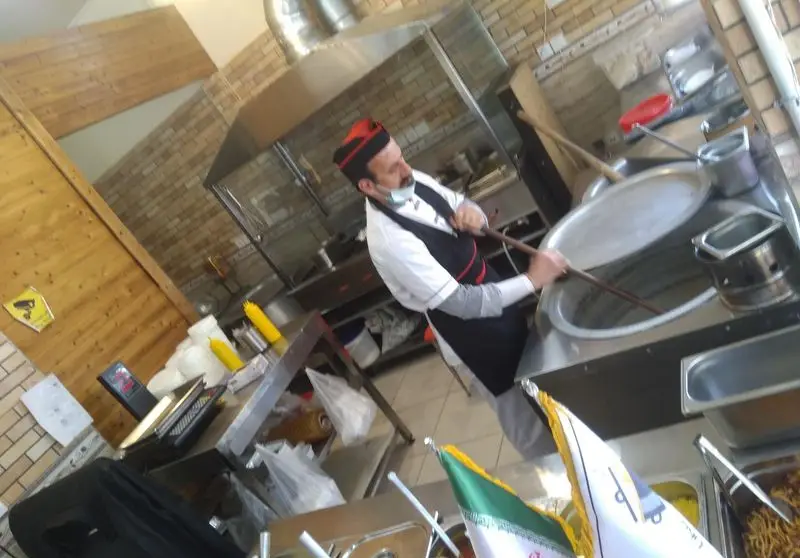 سرآشپز حرفه‌ای رستوران غذای خونگی فود شادان در حال پخت غذای تازه و اصیل ایرانی در آشپزخانه‌ای تمیز و مجهز با دیگ‌های بزرگ.