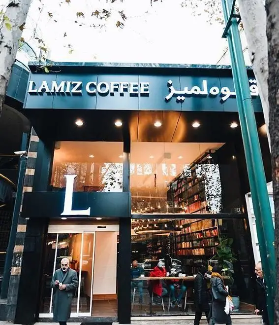 نمای بیرونی کافه قهوه لمیز (Lamiz Coffee) در باغ فردوس با تابلوی روشن، پنجره‌های بزرگ، قفسه‌های کتاب و مشتریان.