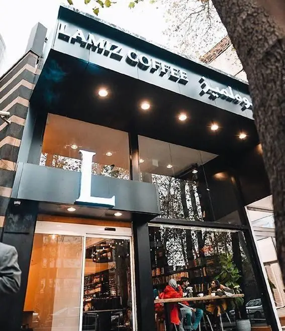 نمای بیرونی کافه قهوه لمیز باغ فردوس تهران، با تابلوی "L'AMIZ COFFEE" و طراحی مدرن، ورودی شیشه‌ای و فضای دنج داخلی.