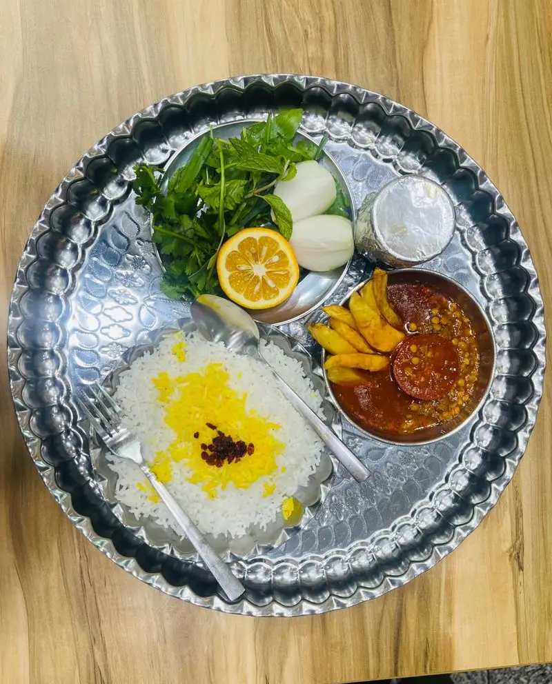 یک سینی کامل غذای اصیل ایرانی از رستوران دایی دیزی شامل پلو زعفرانی، خورشت قیمه با سیب‌زمینی و سبزی تازه.