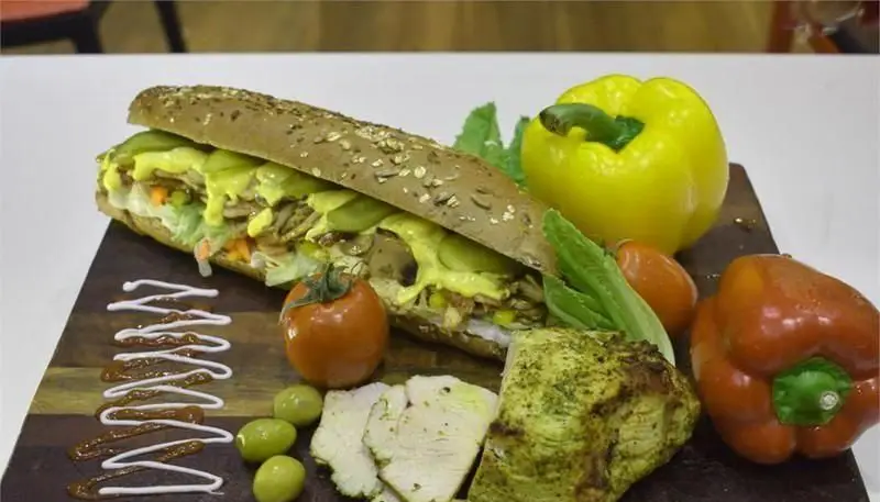 ساندویچ ساب حجیم و لذیذ، حاوی مرغ گریل، سس مخصوص و سبزیجات تازه، به همراه فلفل دلمه، زیتون و برش‌های بوقلمون. منوی کامل بستنی ایوب.
