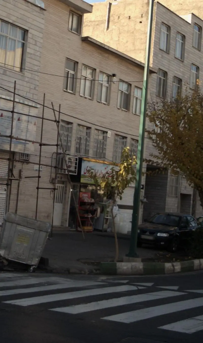 نمایی از مغازه لبنیات سنتی دامداران یزدی در خیابان شلوغ، با داربست مقابل ساختمان و خودرویی پارک شده در کنار پیاده‌رو.