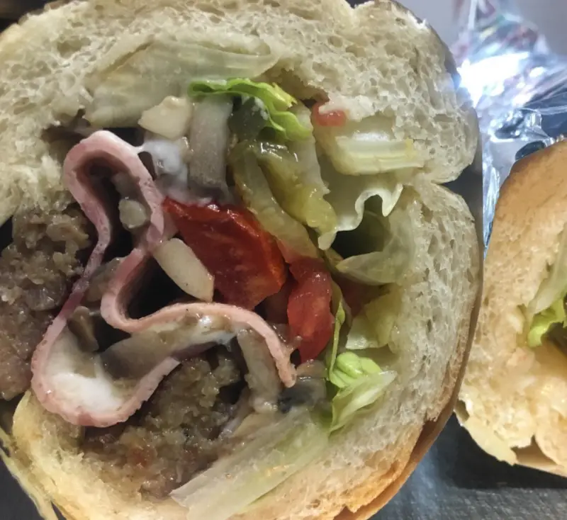 تصویری وسوسه‌انگیز از برش عرضی ساندویچ فلافل نیم متری بابی با نان باگت، شامل فلافل، کاهو، گوجه، قارچ، ترشی و سس.