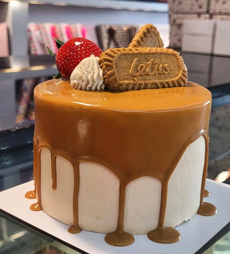 کیک خوشمزه کارامل و لوتوس بیسکوییت با تزیین توت فرنگی از شیرینی سوییت پالاس، ایده‌آل برای جشن‌ها و سفارش آنلاین دسر.