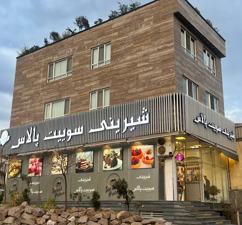 نمای بیرونی شیرینی و قنادی سوییت پالاس، ساختمانی با نمای سنگ مدرن، تابلوی بزرگ نورانی و تصاویر جذاب انواع دسر و شیرینی.