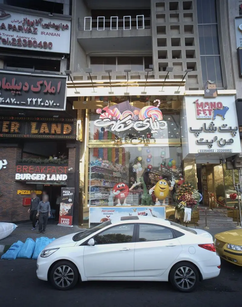 تصویری از نمای بیرونی دنیای شکلات اندرزگو، فروشگاه تخصصی شکلات و آبنبات با ویترین رنگارنگ، در کنار پت شاپ و برگر لند.