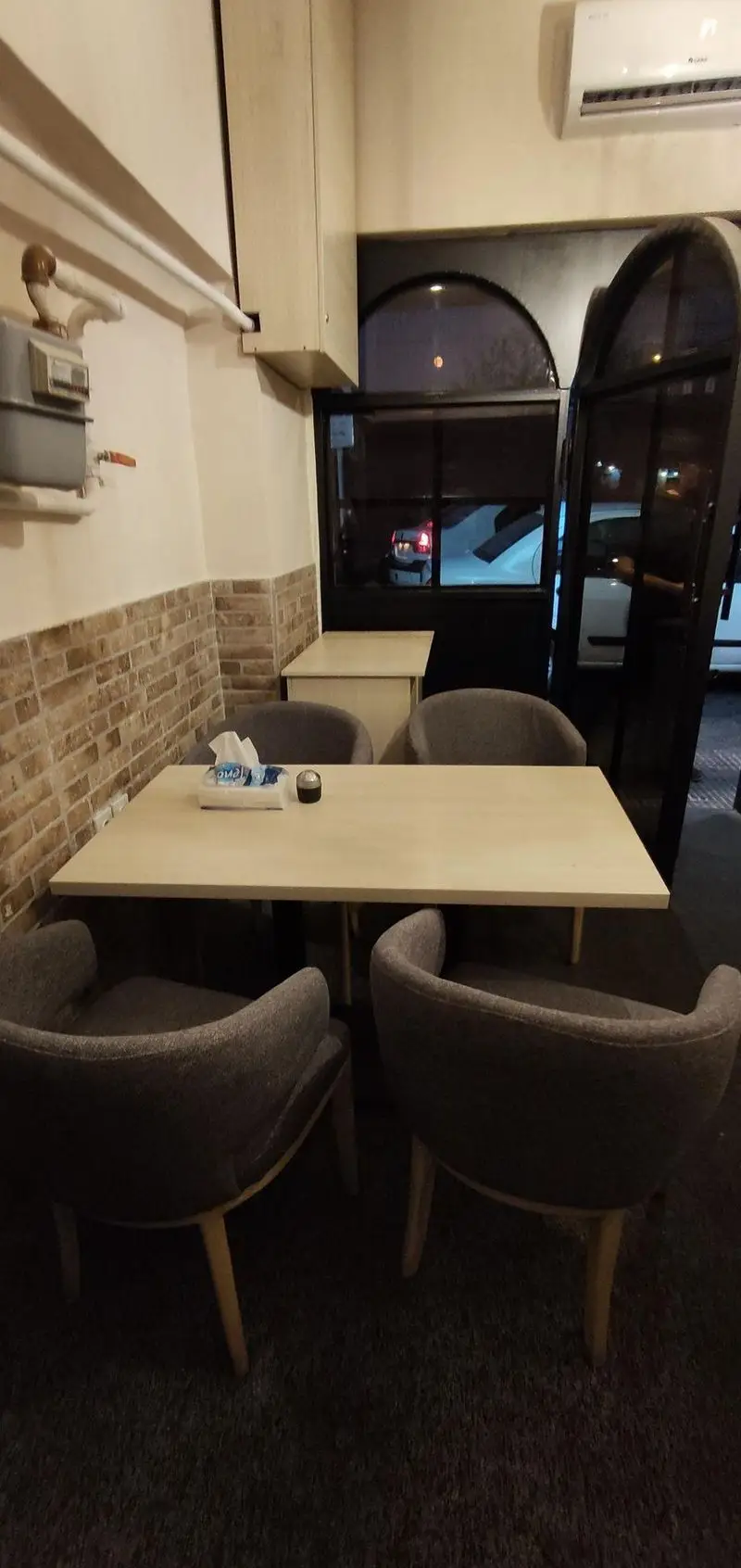 فضای دنج و مدرن داخلی رستوران سید جلال: میز غذاخوری چهارنفره با صندلی‌های راحت، دیوار آجری و منظره شب از پنجره.