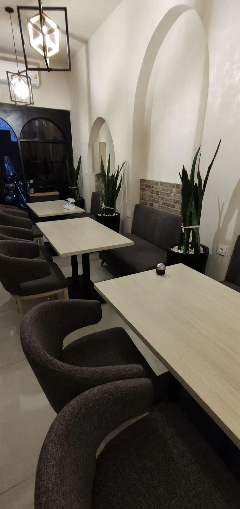 نمای داخلی رستوران و کافه سید جلال با دکوراسیون مدرن، میزهای چوبی روشن، صندلی‌های پارچه‌ای دنج، دیوارهای آجری و طاق‌دار و گیاهان بلند.