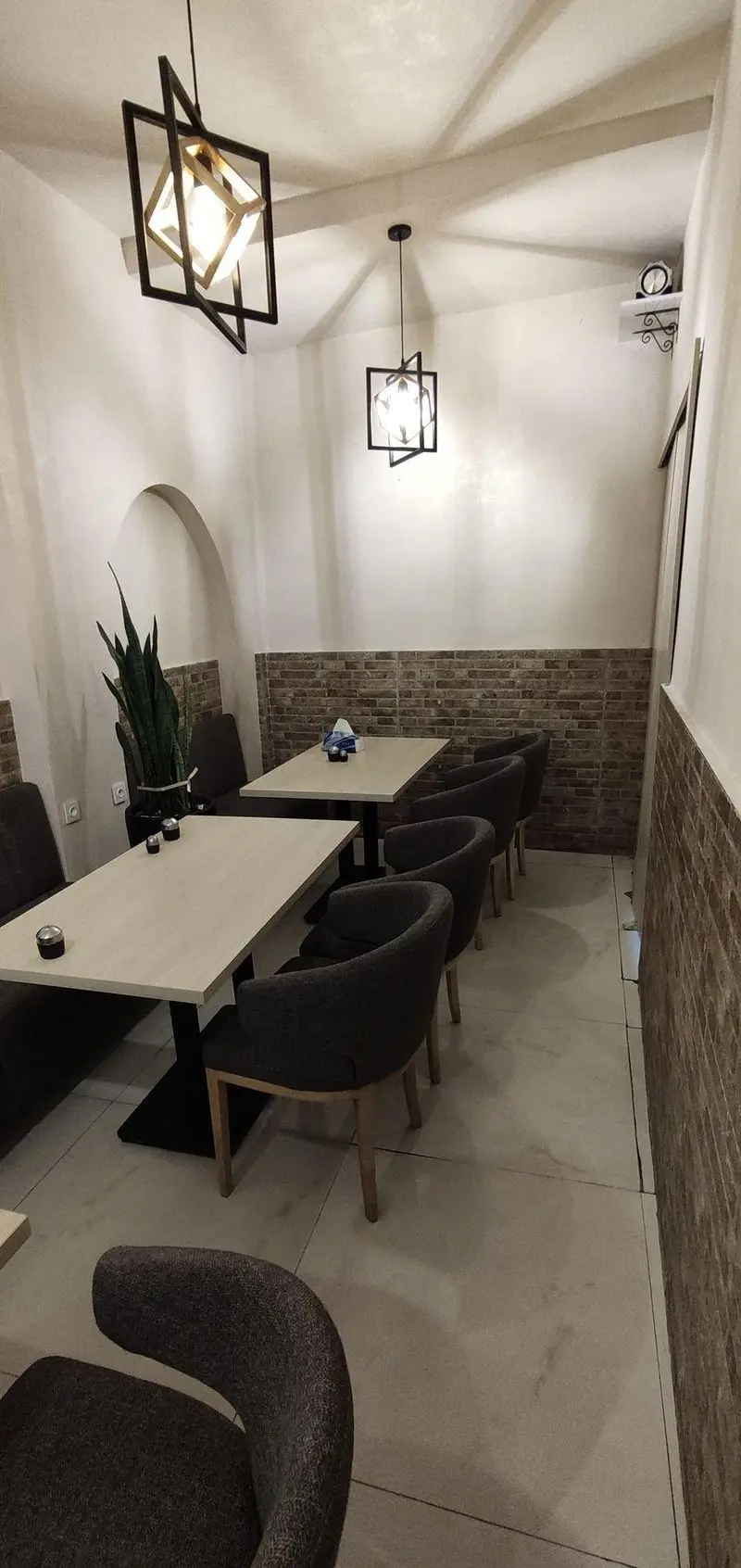 محیط داخلی رستوران سید جلال با دکوراسیون مدرن شامل میزهای چوبی روشن، صندلی‌های راحت، نورپردازی سقفی هندسی و دیوارهای ترکیبی آجر و سفید.