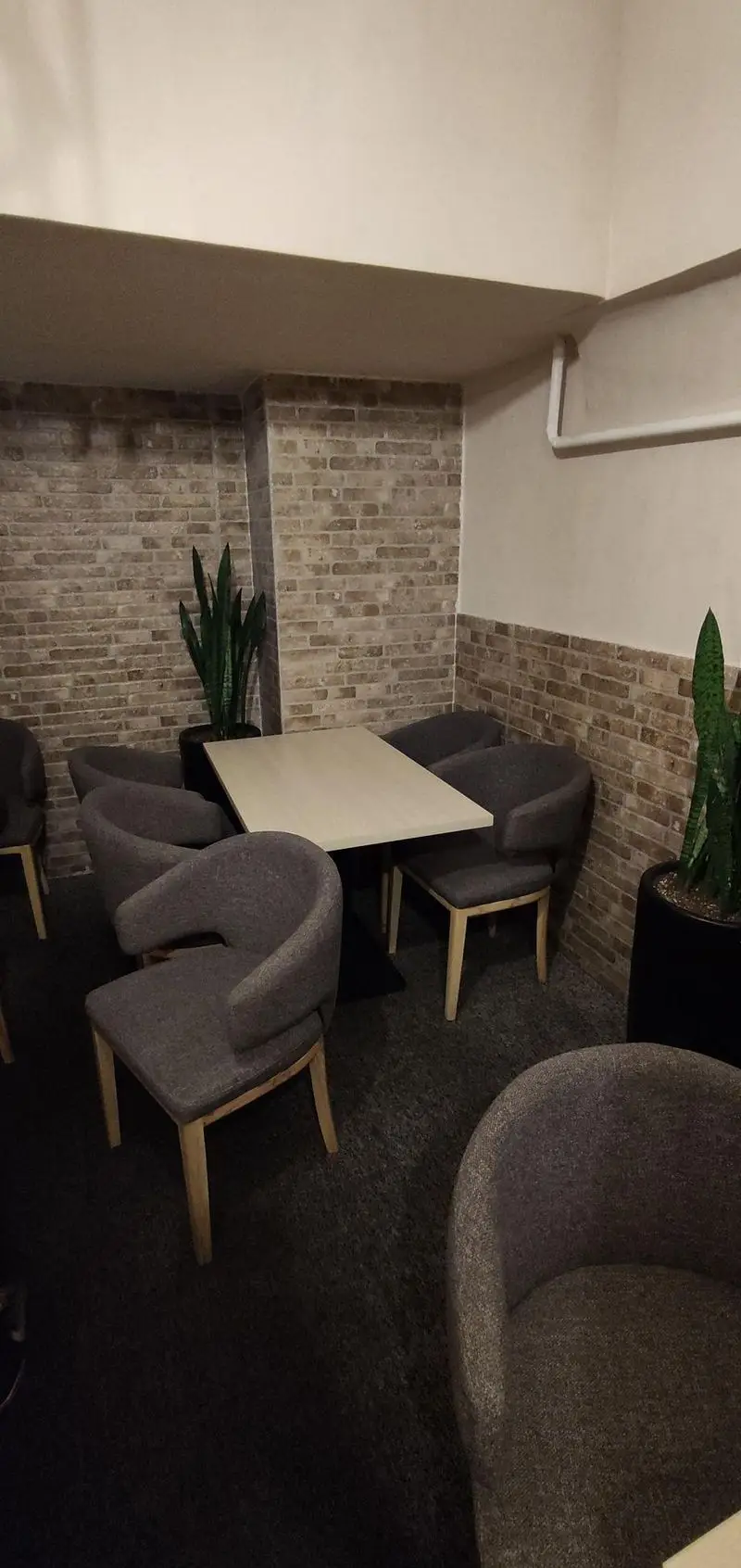 فضای داخلی دنج رستوران سید جلال با میز و صندلی‌های طوسی مدرن، دیوارهای آجری، کفپوش موکت و گلدان‌های طبیعی برای تجربه‌ای دلپذیر.