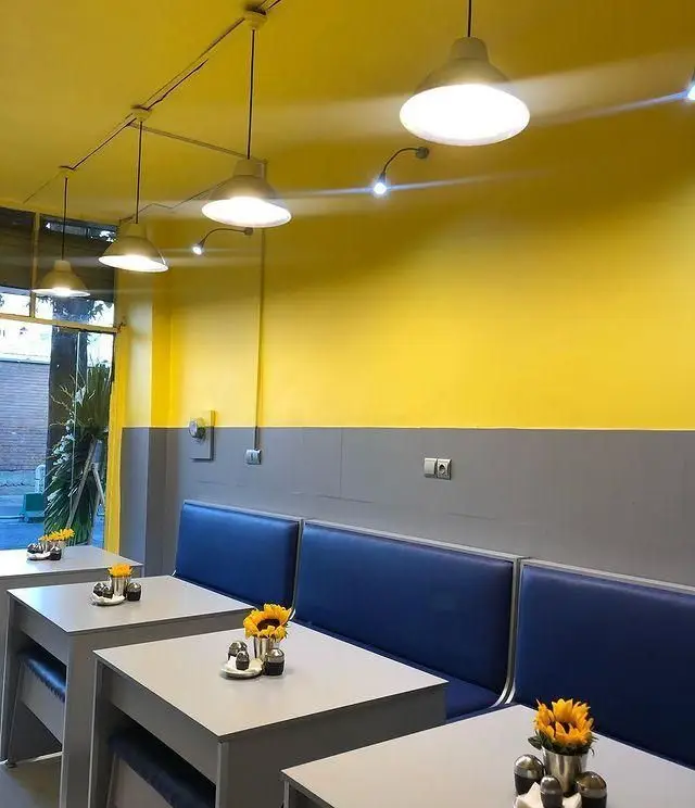 دکوراسیون داخلی مدرن رستوران سید جلال با دیوار زرد، نیمکت‌های آبی، میزهای روشن و گل‌های آفتابگردان برای فضایی دلنشین و شیک.