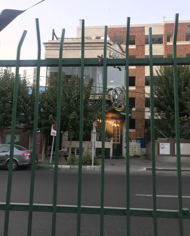 نمای بیرونی رستوران ایتالیایی تیپو با نمای شیک و مدرن، فضای دلنشین و تابلوهای نورانی، از پشت نرده‌های سبز در تهران.