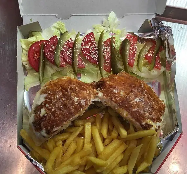 ساندویچ بزرگ و خوشمزه فست فود چهار پنج شش با پنیر ذوب شده، سیب زمینی سرخ کرده، کاهو، گوجه و خیارشور.