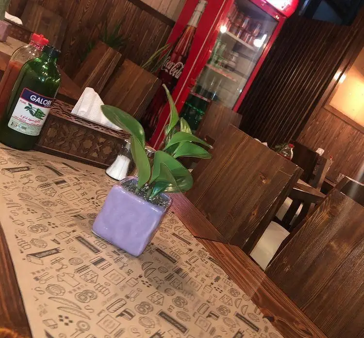 محیط داخلی دلنشین و دنج فست فود کاپو پیتزا با میز و صندلی چوبی، تزیینات میز و یخچال کوکاکولا در پس زمینه.