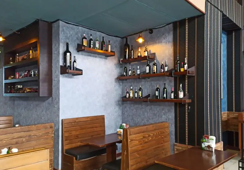 نمای داخلی رستوران فست فود گزینگ برگر، با طراحی مدرن و دلنشین، قفسه‌های دیواری چوبی مزین به بطری‌های دکوراتیو و مبلمان چوبی راحت.
