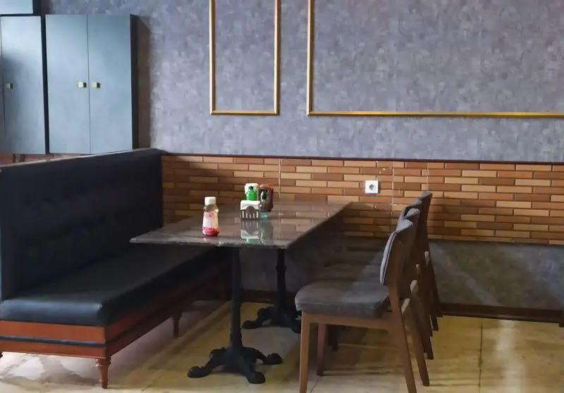 فضای داخلی مدرن و شیک فست فود گزینگ برگر با میز و صندلی‌های راحت، نیمکت، دیوار آجری و قاب‌های طلایی، محیطی دلپذیر برای مشتریان.