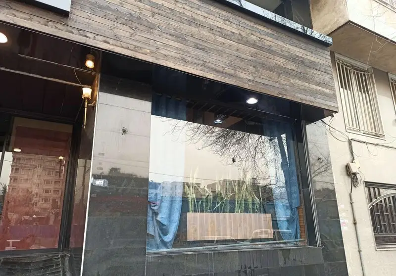 ورودی شیک فست فود گزینگ برگر با پنجره‌های بزرگ و نمای چوبی. دکوراسیون داخلی با گیاهان سبز و نورپردازی گرم از پشت شیشه قابل مشاهده است.