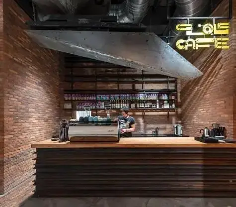 فضای داخلی کافه فلو در آوا سنتر با طراحی صنعتی، دیوارهای آجری، کانتر چوبی، باریستا و تجهیزات مدرن قهوه.