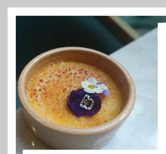دسری زیبا و دلنشین در کافه لوما؛ یک کرم بروله طلایی با رویه‌ی کاراملی و گل‌های بنفش خوراکی. تجربه‌ای خاص و شیرین.