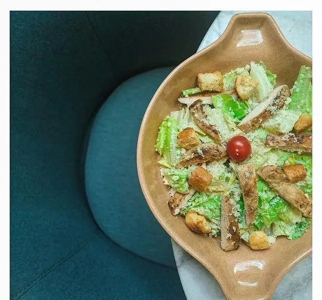 سالاد سزار با مرغ گریل و کروتون در کاسه‌ای شیک روی میز مرمر کافه لوما. غذایی سالم و محبوب برای تجربه‌ای دلپذیر در رستوران.