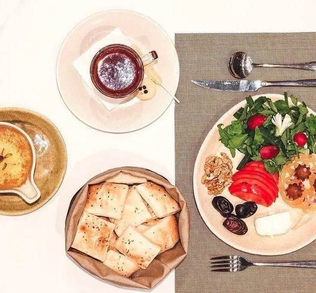 میز صبحانه کافه لوما با سالاد تازه، نان داغ، پنیر، گردو، زیتون، گوجه و چای. یک غذای سالم و خوشمزه برای شروع روز.