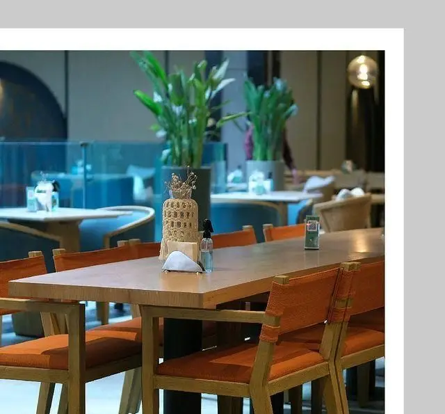 دکوراسیون داخلی زیبا و مدرن کافه لوما، دارای میزهای چوبی بزرگ، صندلی‌های راحت نارنجی، گلدان‌های گیاه سبز و فضایی دلنشین و آرام.