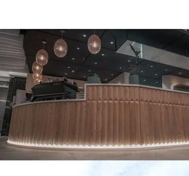 کانتر چوبی منحنی و مدرن کافه لوما با نورپردازی زیرین و لوسترهای آویز زیبا، فضایی دلنشین برای مشتریان ایجاد کرده است.