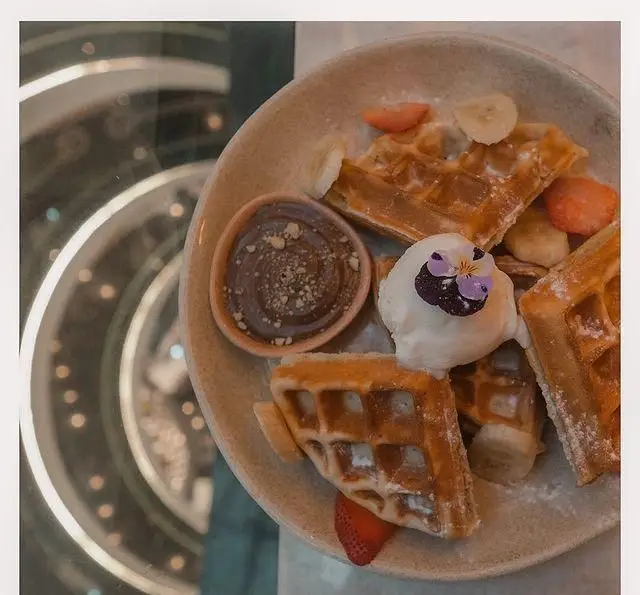 وافل‌های خوشمزه کافه لوما با بستنی و میوه‌های تازه (موز و توت فرنگی)، دسری شیرین برای تجربه‌ای دلنشین در کافه‌ای جذاب.