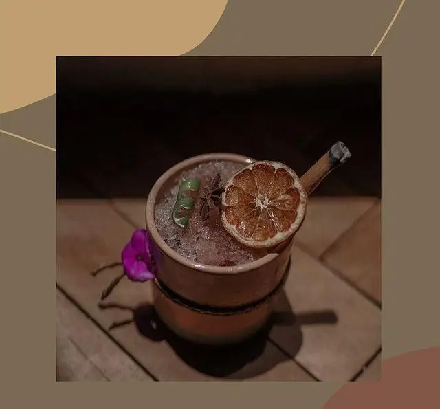 نوشیدنی کوکتل ویژه و جذاب کافه لوما با تزئینات هنری نارنج، چوب دارچین و یخ خرد شده، تجربه‌ای لذت‌بخش در کافه.