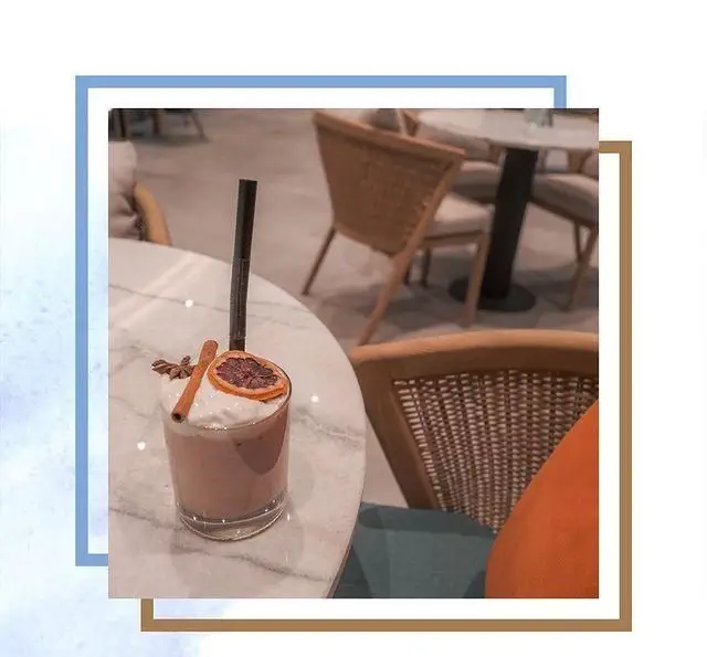 عکس نوشیدنی لذیذ کافه لوما با خامه، دارچین و پرتقال خشک روی میز مرمری سفید در محیط آرام و دکوراسیون لوما.