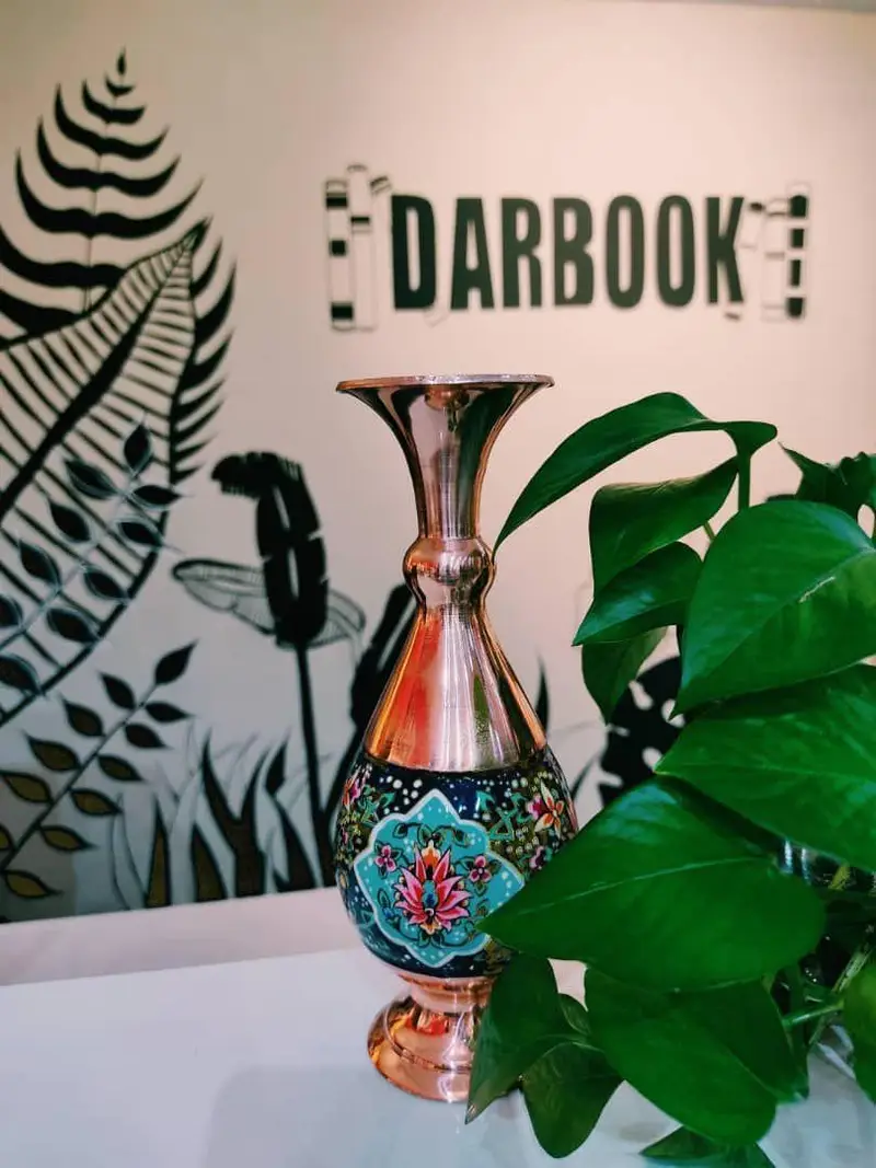 دکوراسیون شیک و فرهنگی فروشگاه کتاب داربوک با گلدان مسی دست‌ساز، نقاشی سنتی ایرانی و گیاه سبز زیبا، مناسب علاقه مندان کتاب.