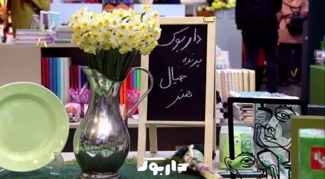 نمایی از فروشگاه کتاب داربوک با گل و تخته سیاه حاوی شعار 'پرنده خیال، هنر'، نمایشگر فضای فرهنگی و هنری کتابفروشی.