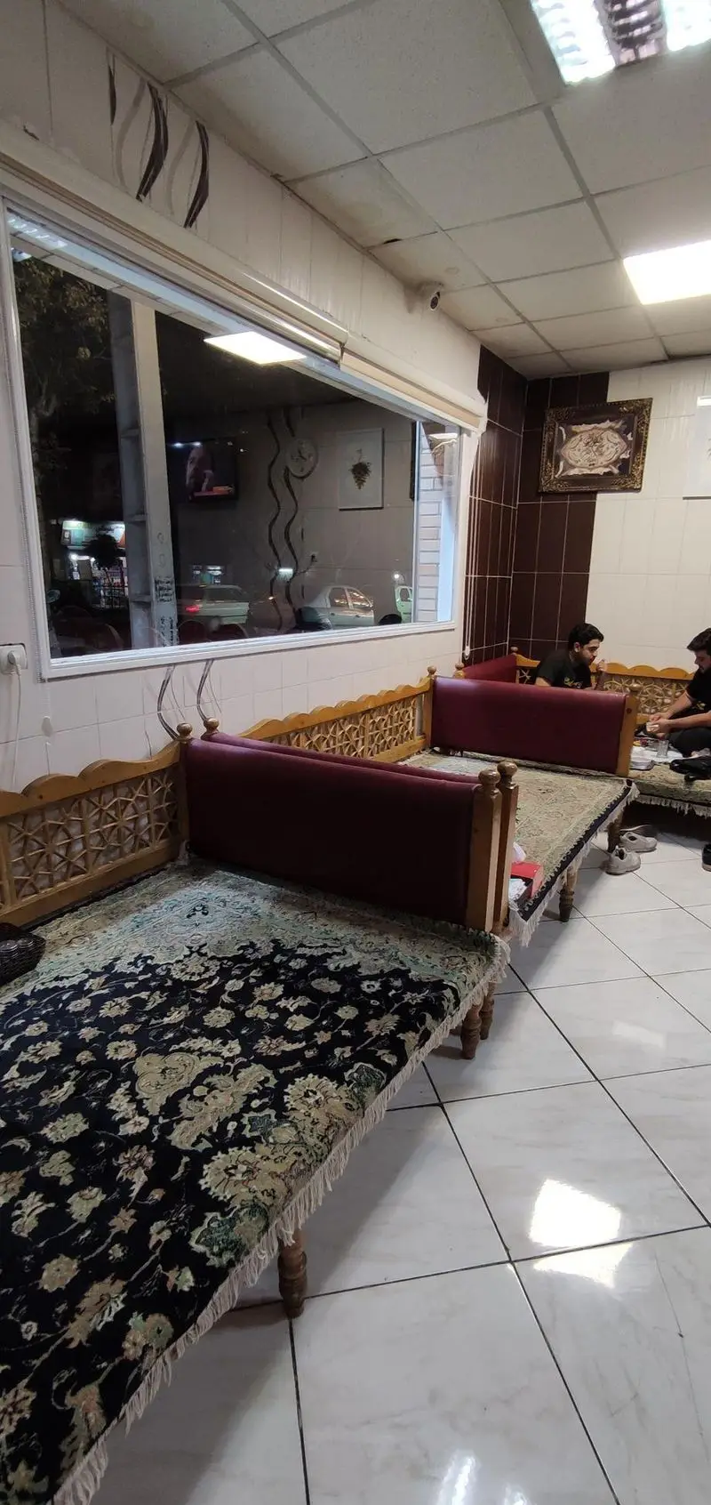 فضای داخلی دنج و سنتی رستوران معلم با تخت‌های چوبی و فرش‌های ایرانی، مناسب برای صرف غذا و دورهمی مشتریان.