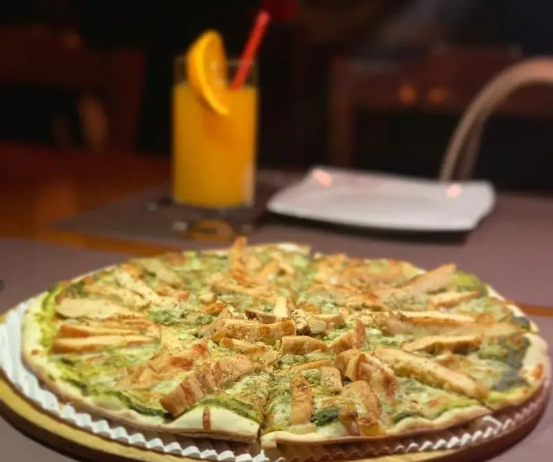 پیتزا مرغ و پستو تازه و خوشمزه رستوران ایتالیایی بلامونیکا، با تکه‌های مرغ گریل شده، ایده‌آل برای یک وعده غذایی دلچسب.