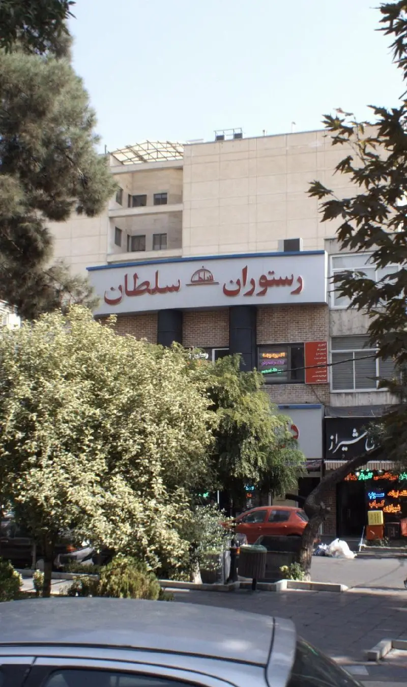 تصویری از نمای بیرونی رستوران سلطان در یک روز آفتابی، با تابلوی بزرگ آن که نام "رستوران سلطان" را نشان می‌دهد، و درختان سبز و خودروها در پیش‌زمینه.